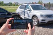 Stressed driver taking picture on sellphone camera of smashed vehicle calling for emergency service help after car accident. Road safety and insurance concept 2104065233