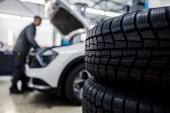 Close up of a new tires in foreground with worker fixing car in blurry background at mechanic's shop. 2248209837