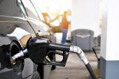 A gasoline pump handle in a gas tank of vehicle with another customer at gas pump in background 2272661533