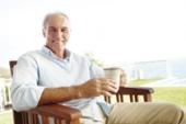 A relaxed mature man sitting on a chair outside drinking coffee