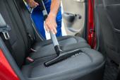 Handyman vacuuming car back seat with vacuum cleaner