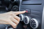 Closeup of young woman pressing emergency button on car sport dashboard.